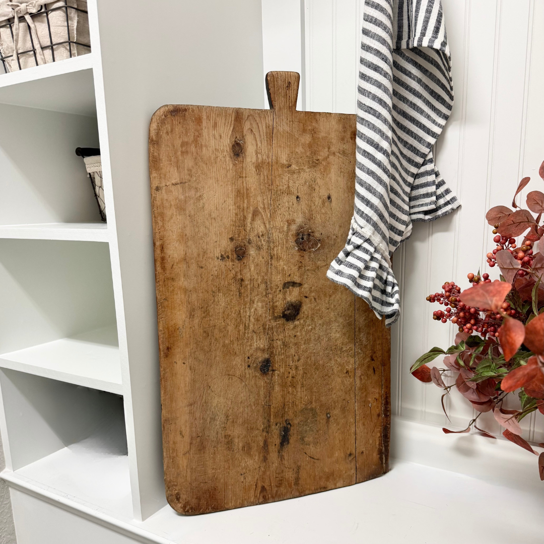 Vintage wooden cutting board on a white surface with a striped towel and flowers in the background.