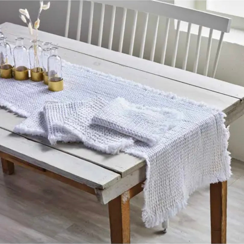 White waffle weave table runner laid out on a wooden table with rustic frayed edges.