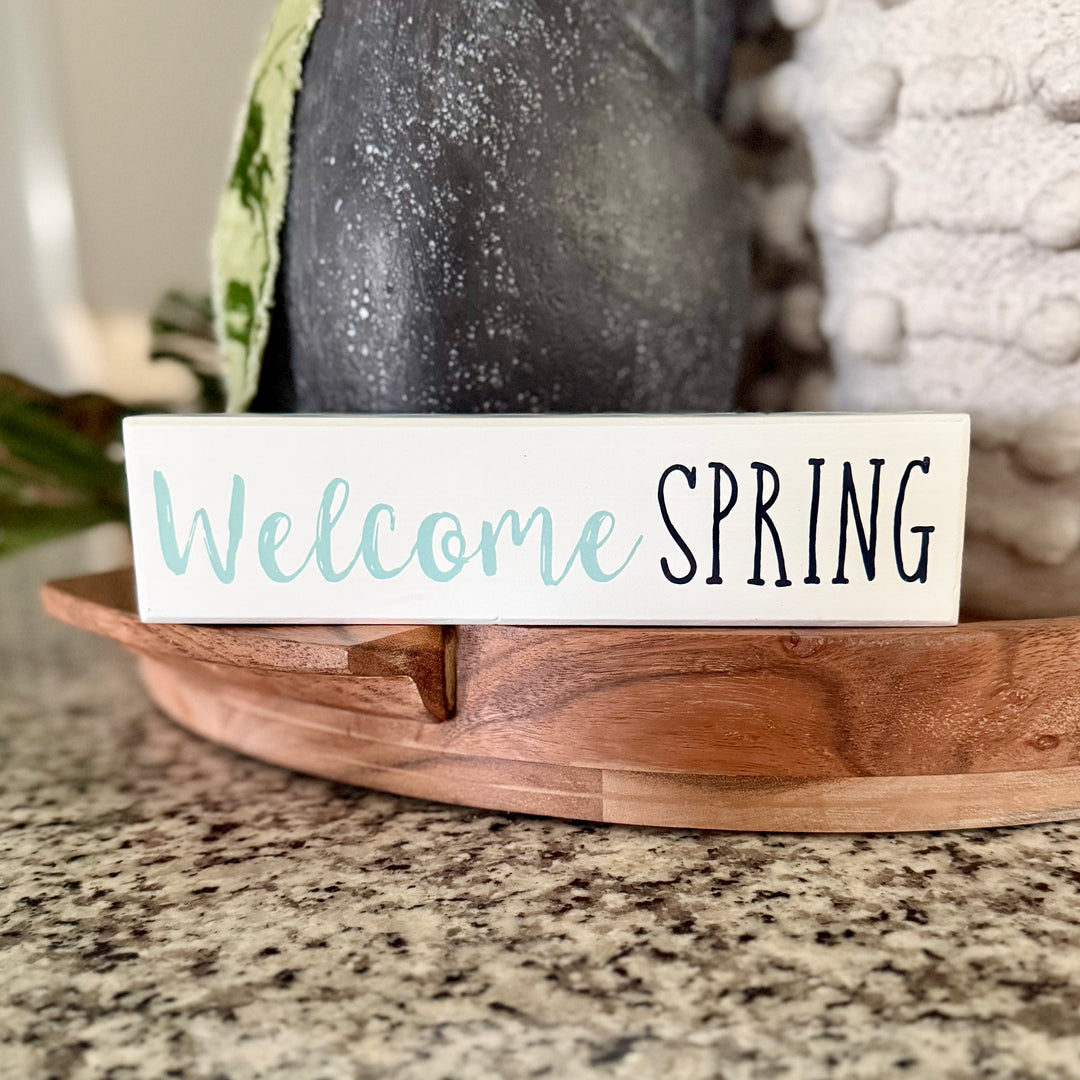 Wooden block with 'Welcome Spring' text on a marble surface