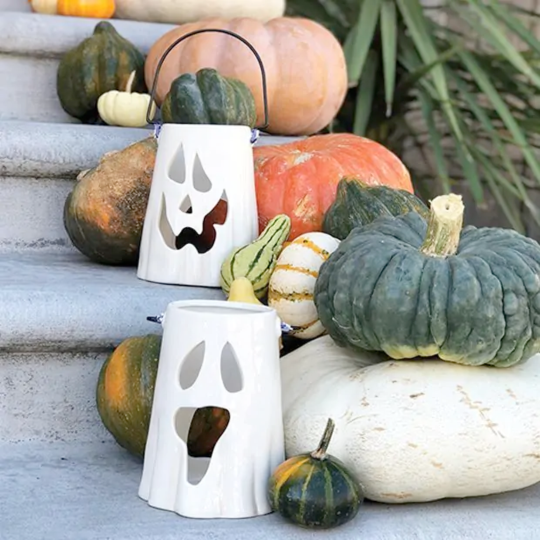 White ghost-shaped candle holders with pumpkins on a stone surface