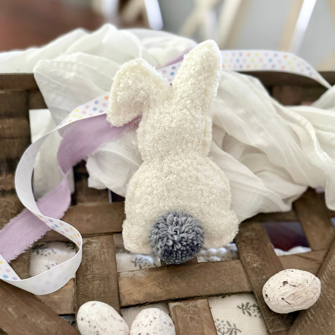 Decorative bunny with pom-pom tail on a wooden surface with ribbons and eggs.