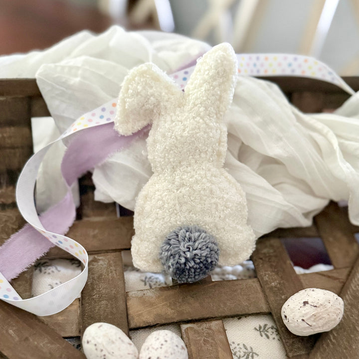 Decorative bunny with pom-pom tail on a wooden surface with ribbons and eggs.