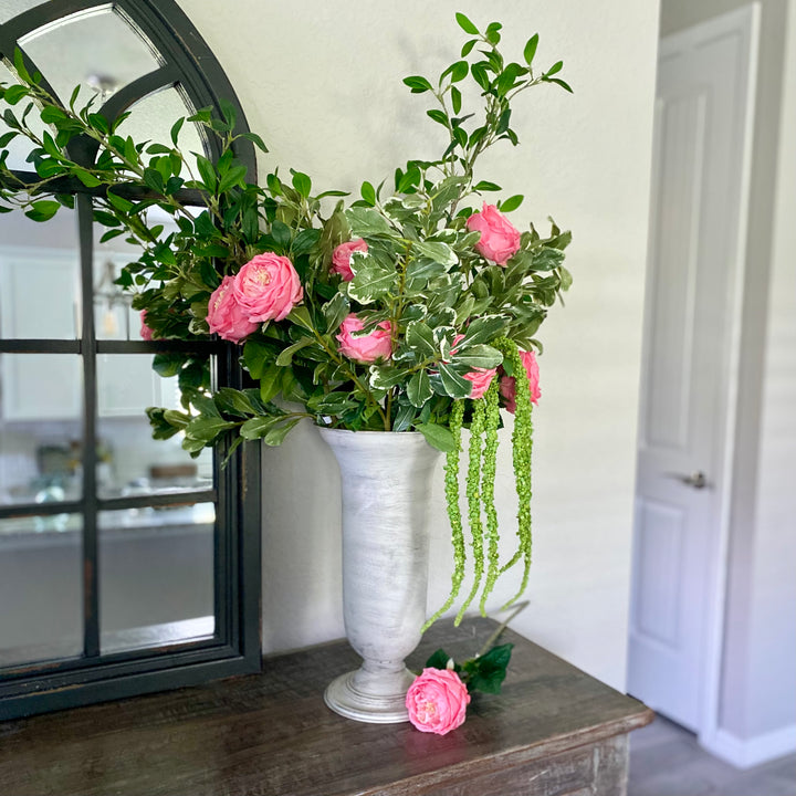 White Fluted Metal Vase with pink roses and greenery on a table.