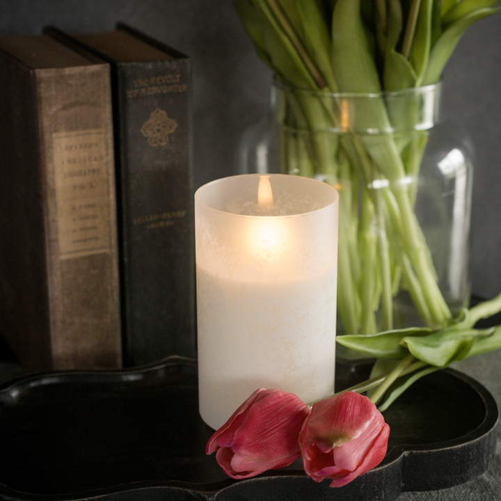 Flameless Candle with a vase of tulips and books on a dark surface