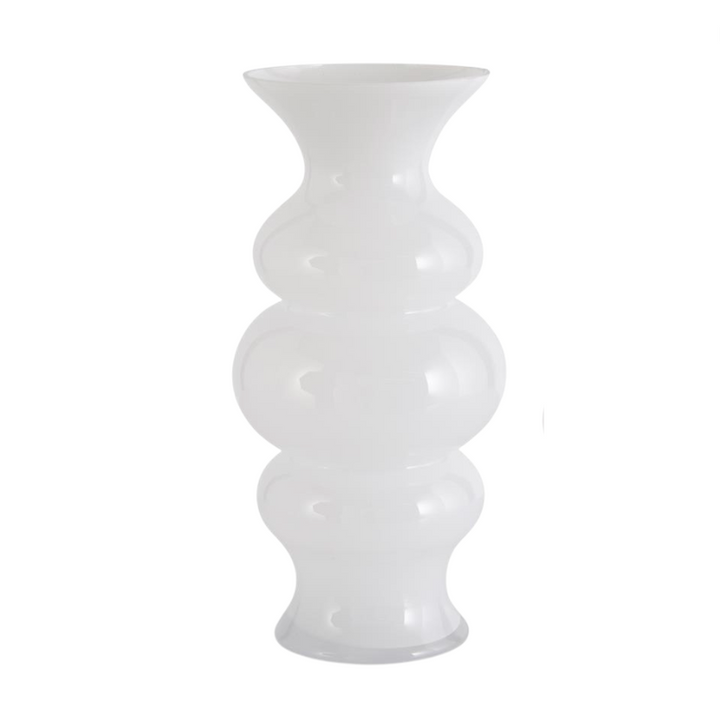 A set of white hourglass fluted glass vases in two sizes displayed on a surface with greenery in the background.