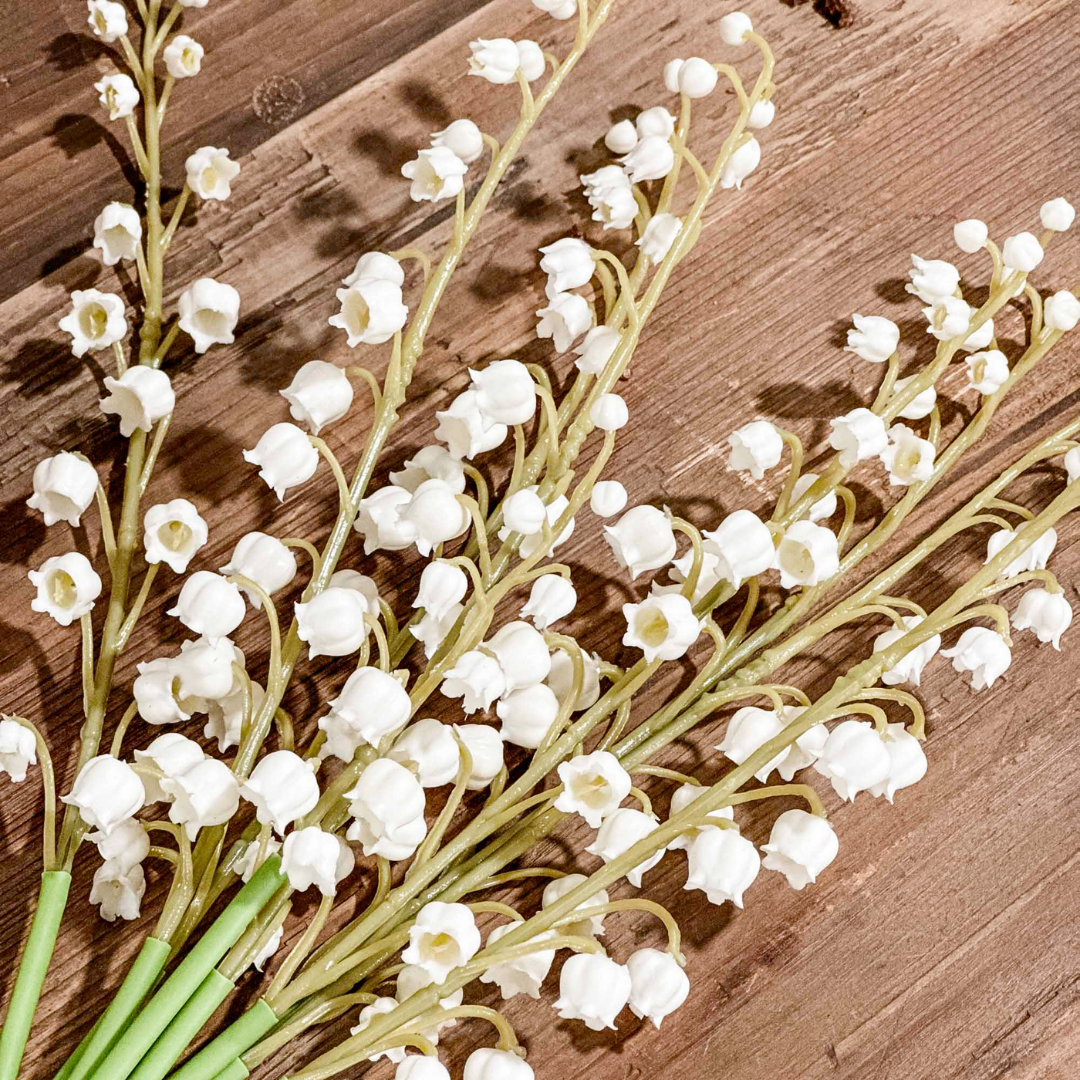 Bouquet of white lily of the valley flowers with green stems on a wooden surface