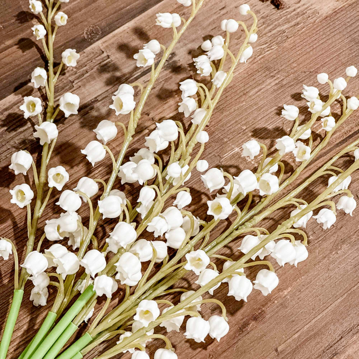 Bouquet of white lily of the valley flowers with green stems on a wooden surface