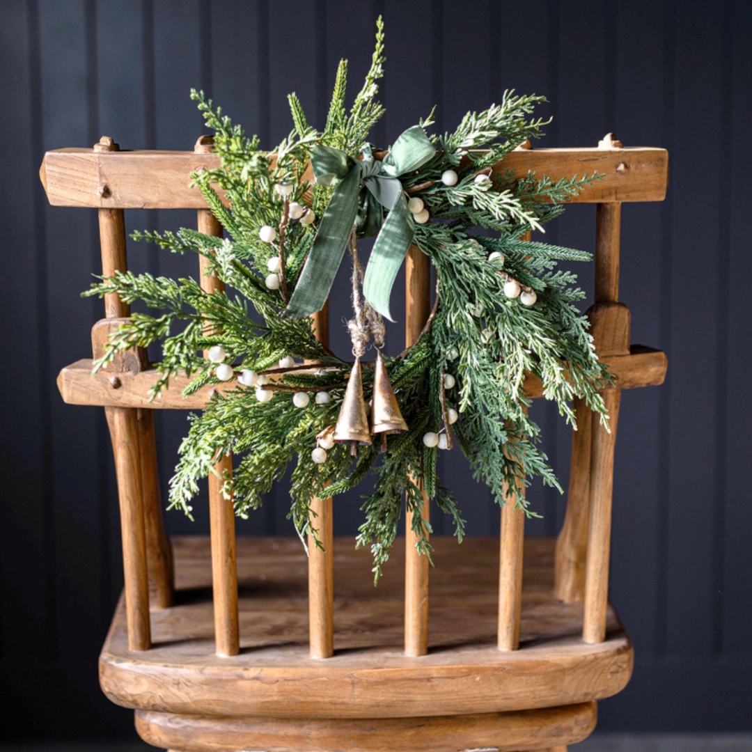 Decorative wreath with greenery and gold bells on a wooden stand against a dark background