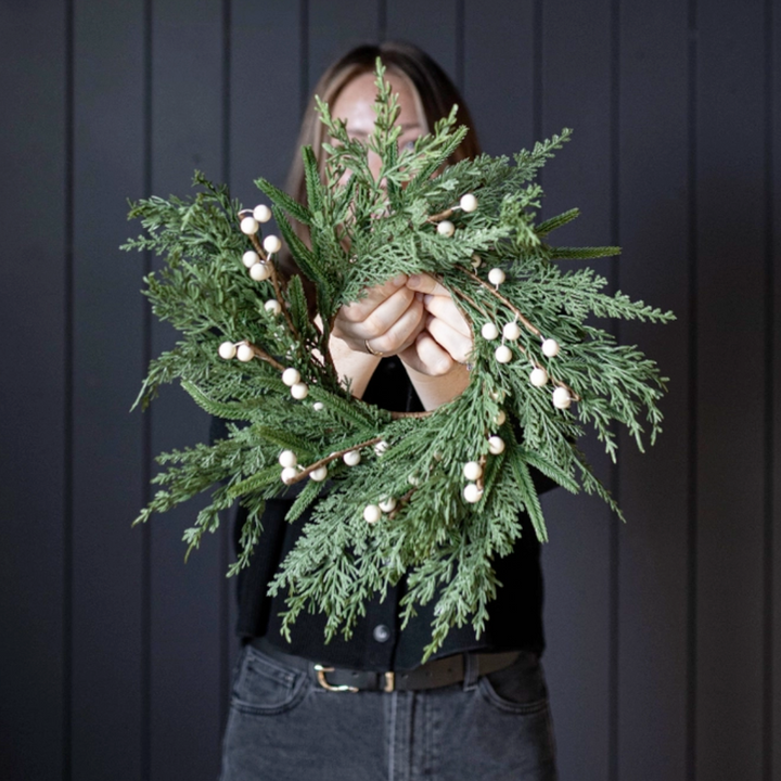 Person holding a green wreath with white berries against a dark background