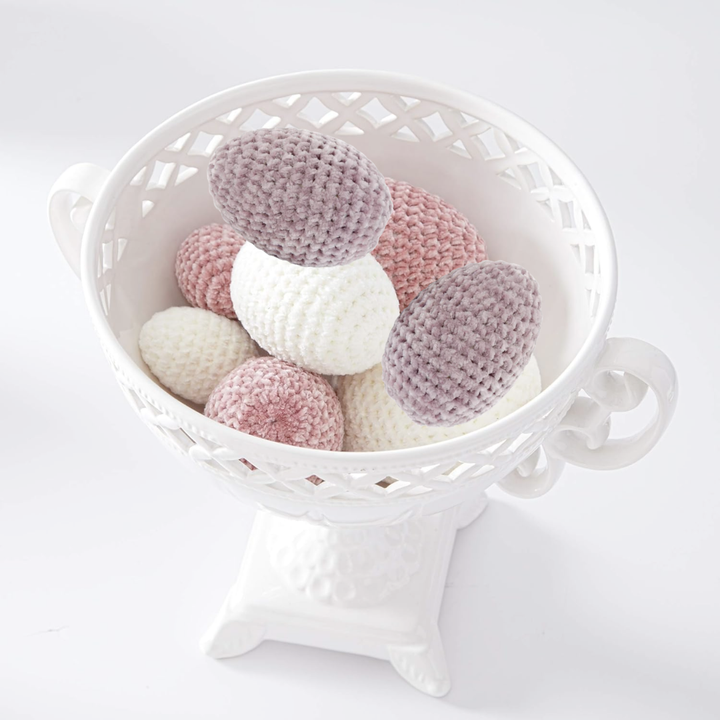 White vase with pink, purple, and white crocheted Easter eggs on a white background