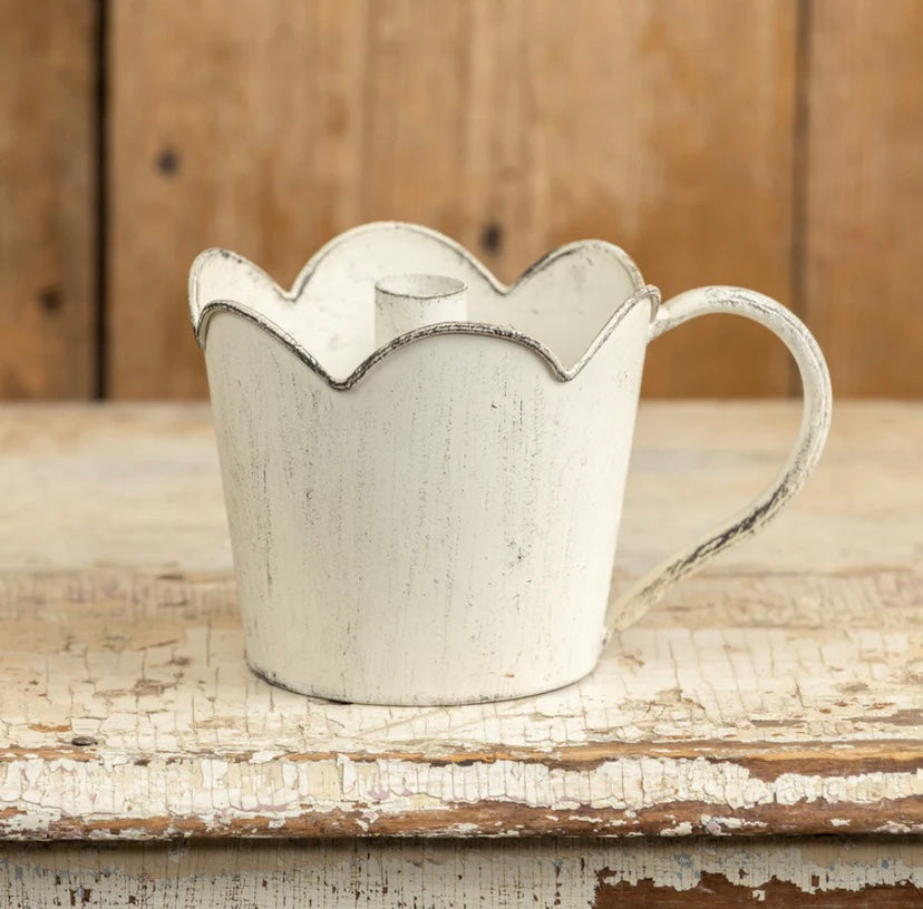 White metal taper candle holder with scalloped edge on a wooden surface