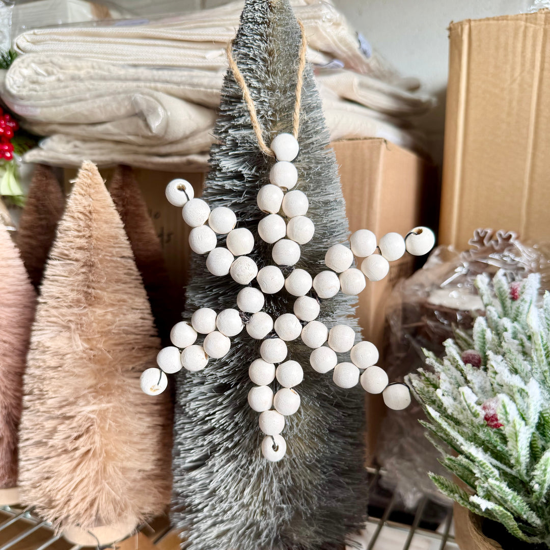Decorative white bead garland on a small tree with Christmas-themed items in the background.