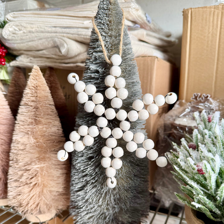 Decorative white bead garland on a small tree with Christmas-themed items in the background.