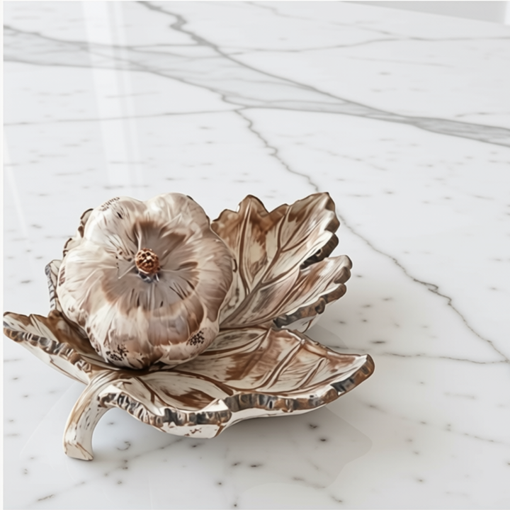 A leaf-shaped resin tray with a textured, organic leaf pattern in earthy brown and cream tones, set on a white marble surface against a white background with a faux feathered pumpkin.