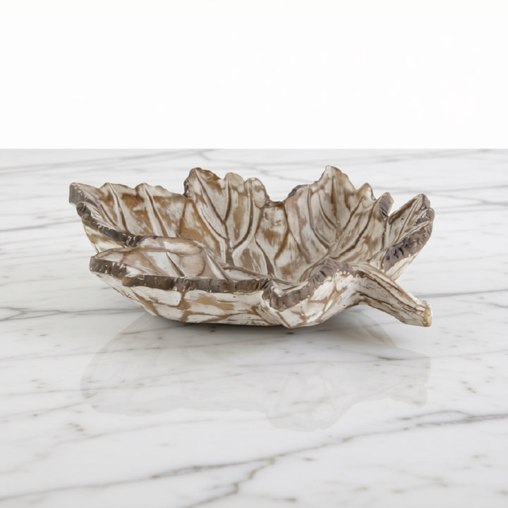 A leaf-shaped resin tray with a textured, organic leaf pattern in earthy brown and cream tones, set on a white marble surface against a white background.