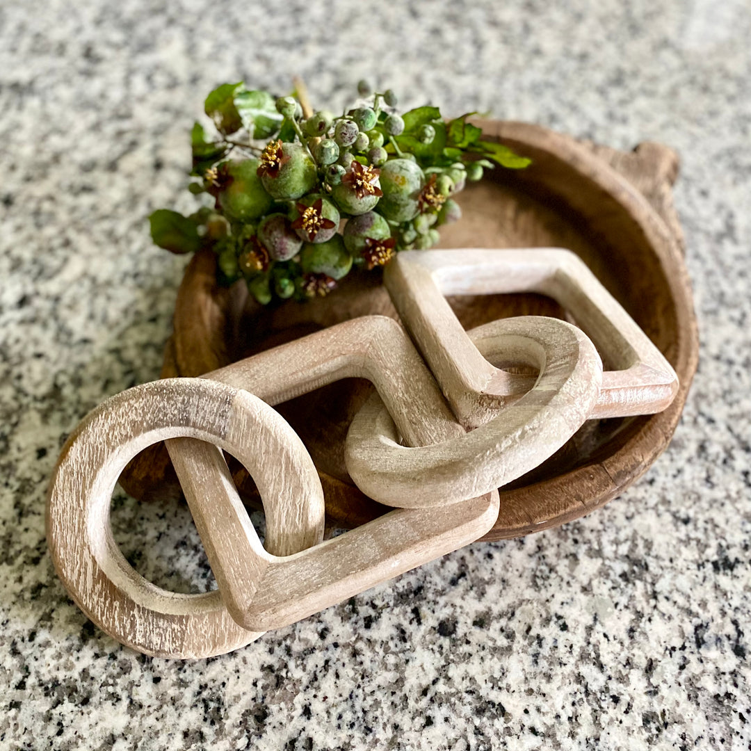 A whitewashed wood link decorative accessory displayed on a round wooden tray with a small green plant on a marble surface.