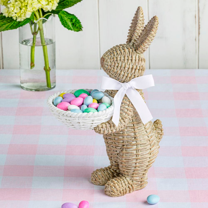Wicker bunny with a basket of colorful eggs on a checkered tablecloth.