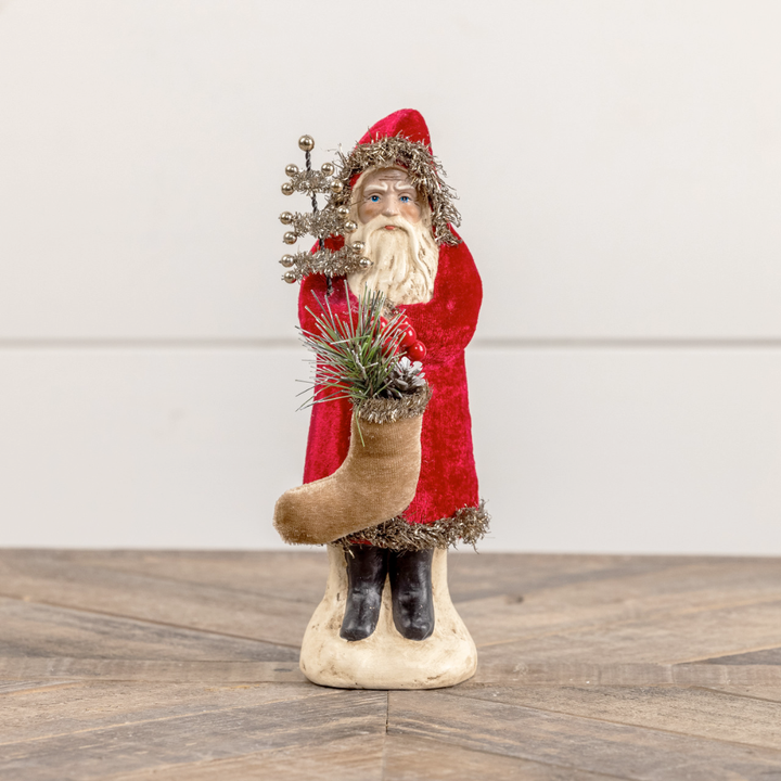 Decorative figure of Santa Claus holding a tree and a stocking on a wooden surface.
