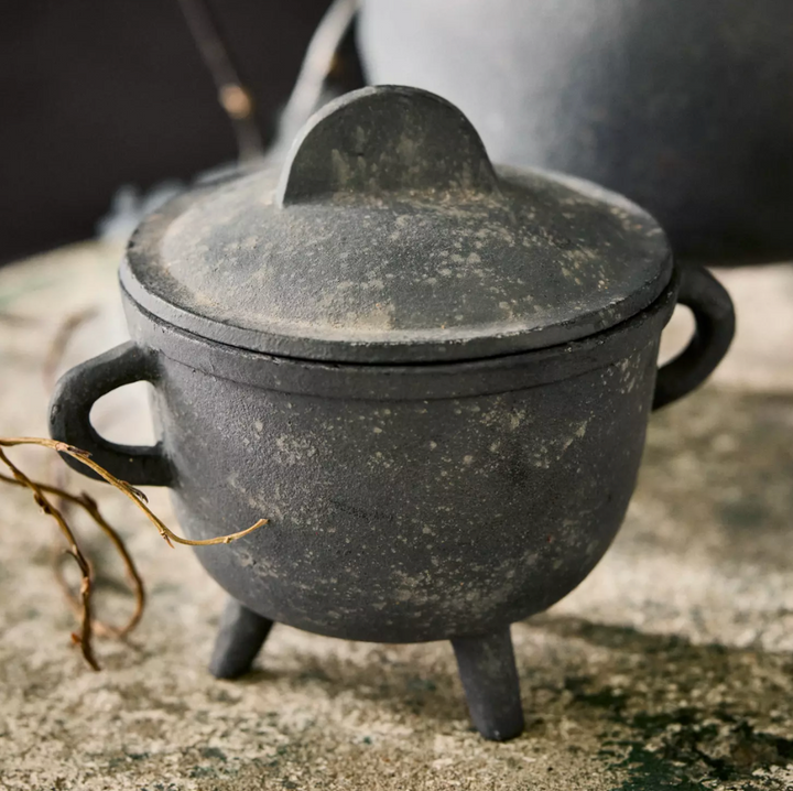 A dark charcoal cast-aluminum tri-fold pot with a matching lid, resting on a textured stone surface.