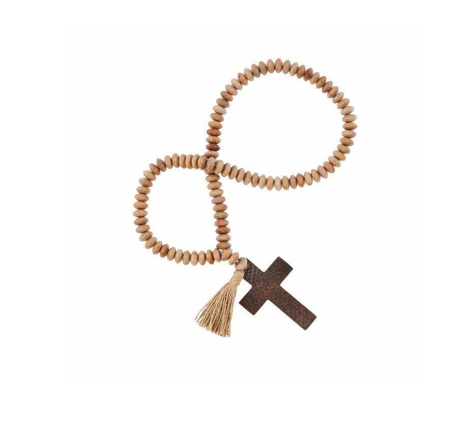 A set of wooden beads with copper-finished pendants and jute tassels, displayed on a wooden surface with books and pine branches.