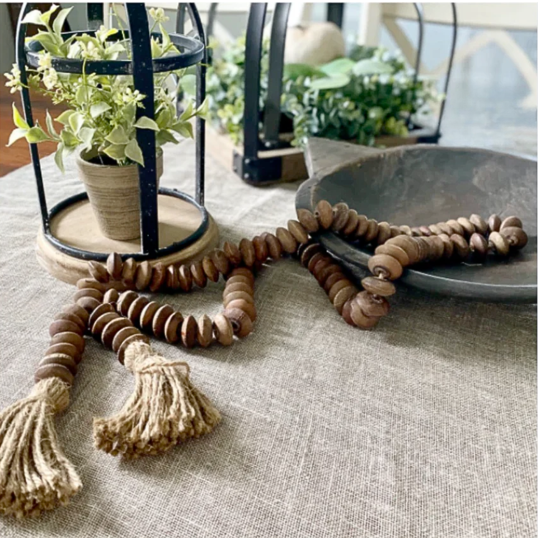 Wooden beaded garland with tassels on a textured surface with plants in the background