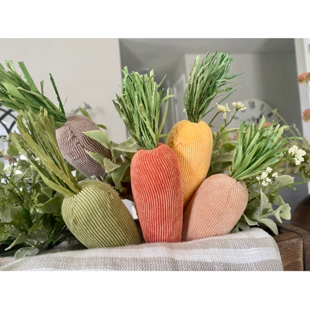 Set of five colorful plush carrot-shaped plush decor with green raffia leaves on a neutral background