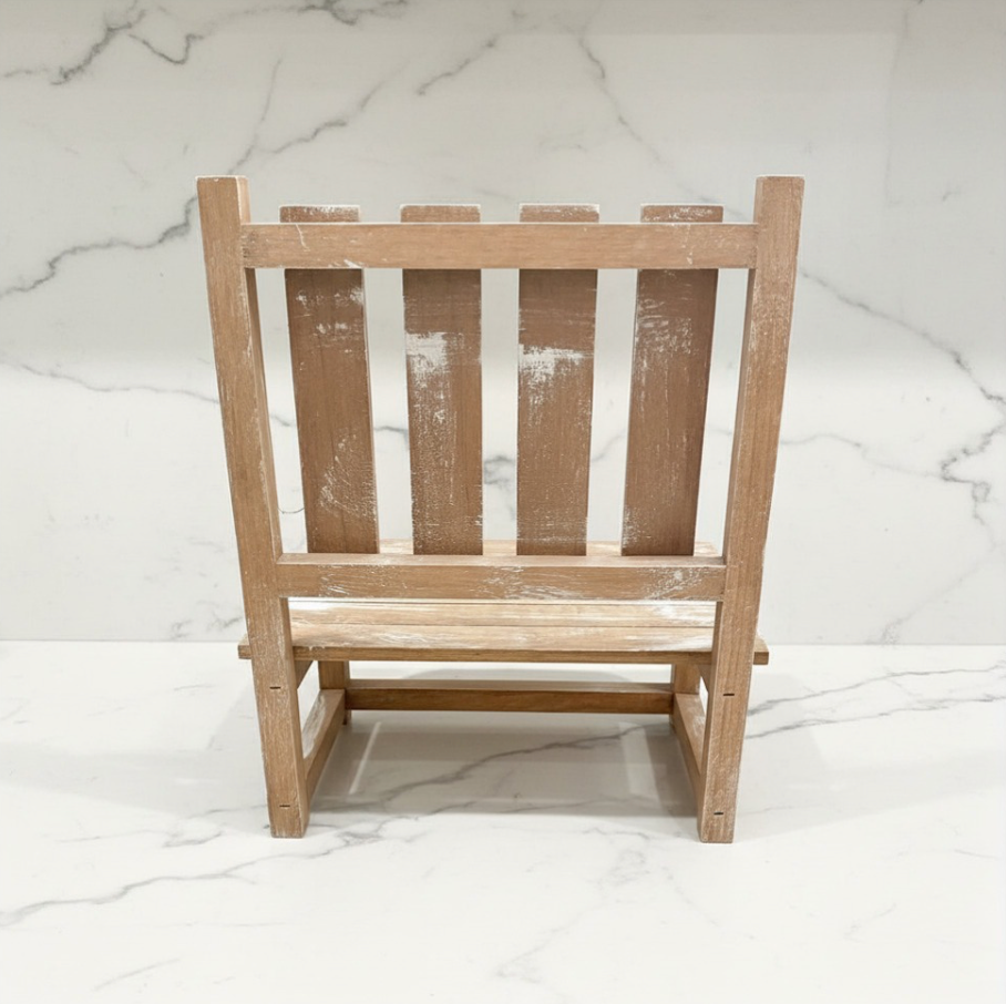 A small wooden dollhouse chair with a distressed, whitewashed finish, shown from the back against a white marble-patterned background.