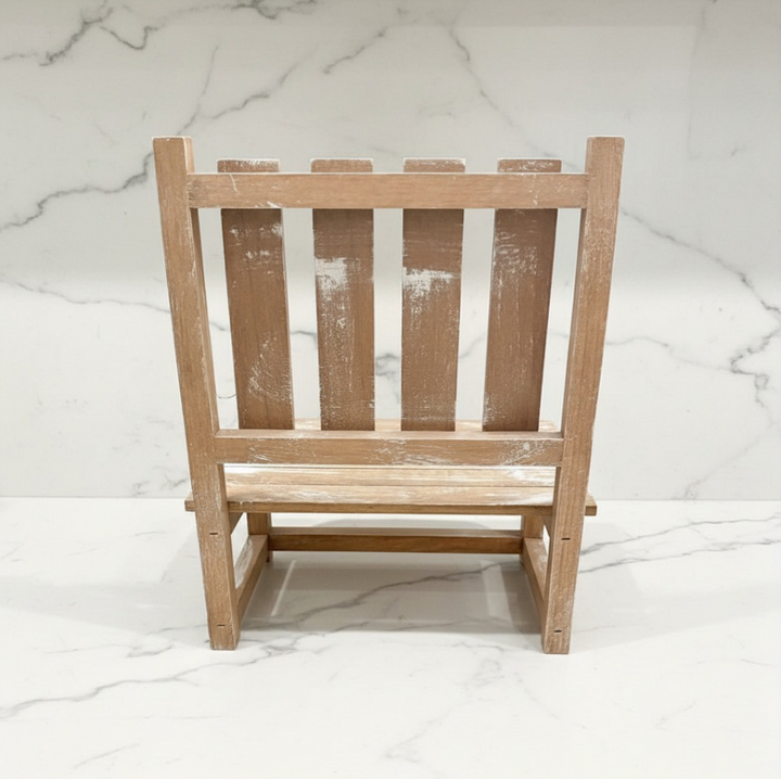 A small wooden dollhouse chair with a distressed, whitewashed finish, shown from the back against a white marble-patterned background.