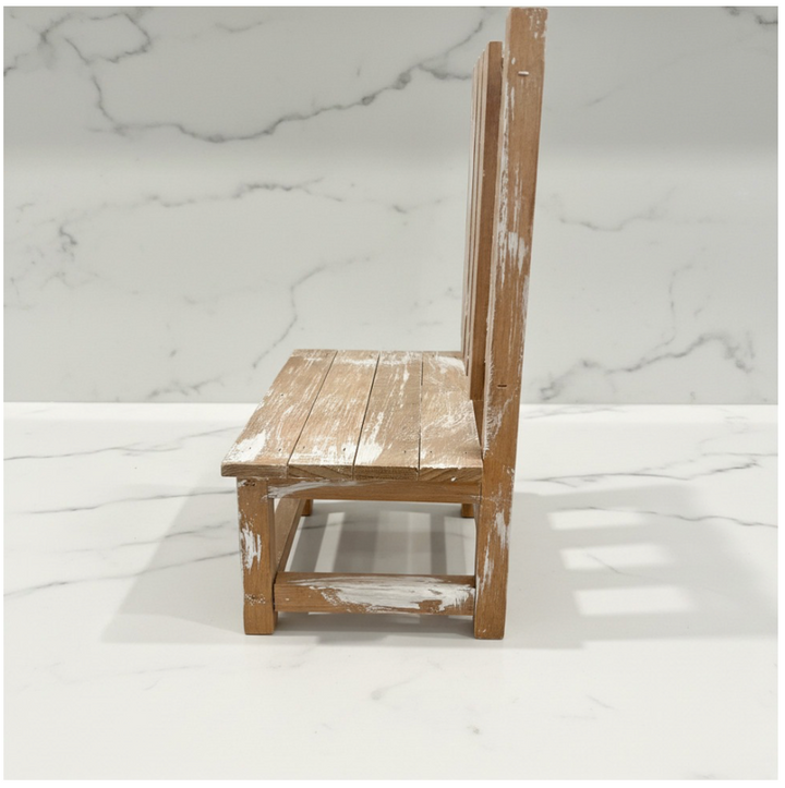 A rustic wooden chair with a distressed white paint finish, shown from a side angle against a white marble-patterned background.