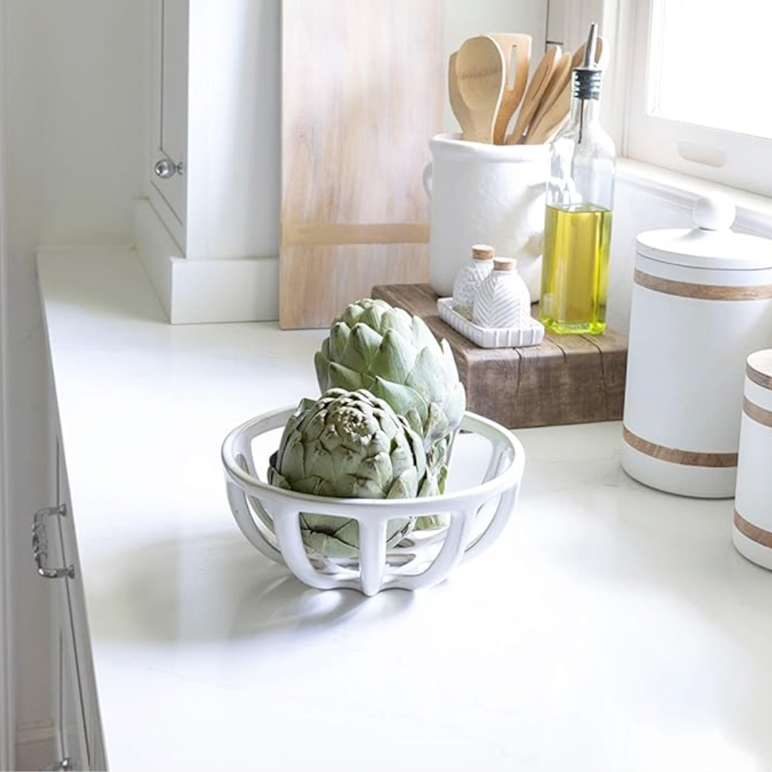 A set of two terracotta fruit baskets, one small inside the other large, with a reactive glaze finish, displayed on a kitchen countertop containing an artichoke.