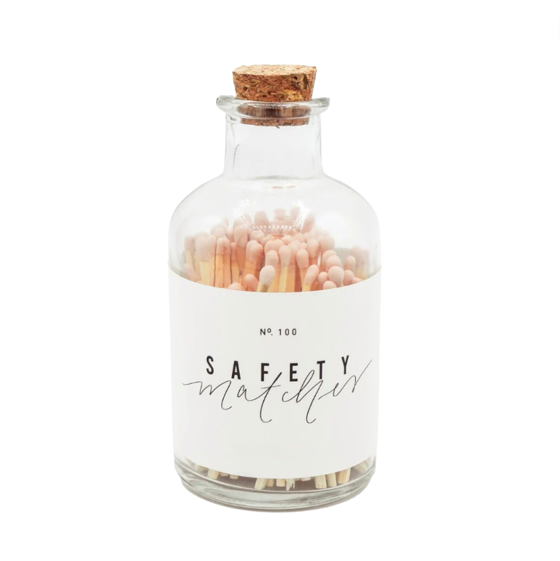 A glass jar with a cork lid labeled 'Safety Matches' containing pink safety matches.