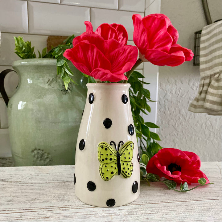 A ceramic Butterfly Mini Vase with black dots and a bright yellow-green butterfly design on a white background, displayed with red flowers.