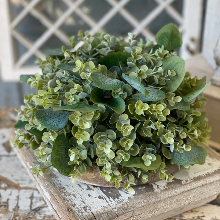 A plastic-made artificial eucalyptus half sphere, displaying a dense arrangement of green leaves, placed on a wooden surface.
