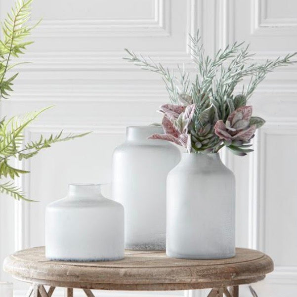 A faux succulent and mixed foliage bundle displayed in a white vase with other potential uses shown in the background.