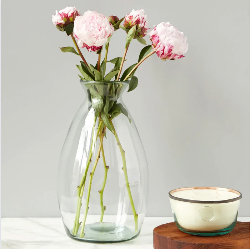 A clear glass vase with a medium height, displaying a bouquet of pink flowers, placed on a wooden surface with a bowl beside it.