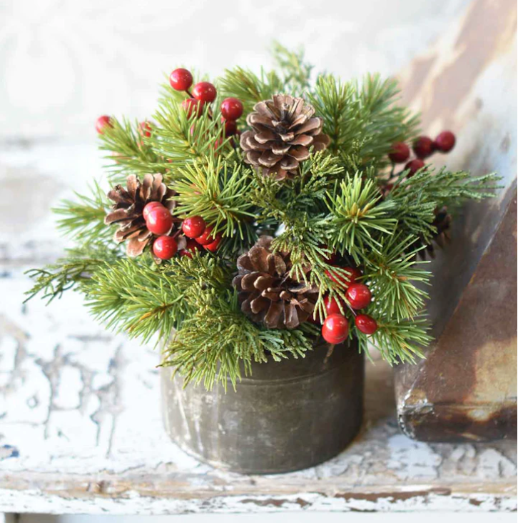 A decorative half sphere made of spruce branches, red berries, and natural pine cones in a Christmas-themed arrangement, placed on a white surface with a textured background.