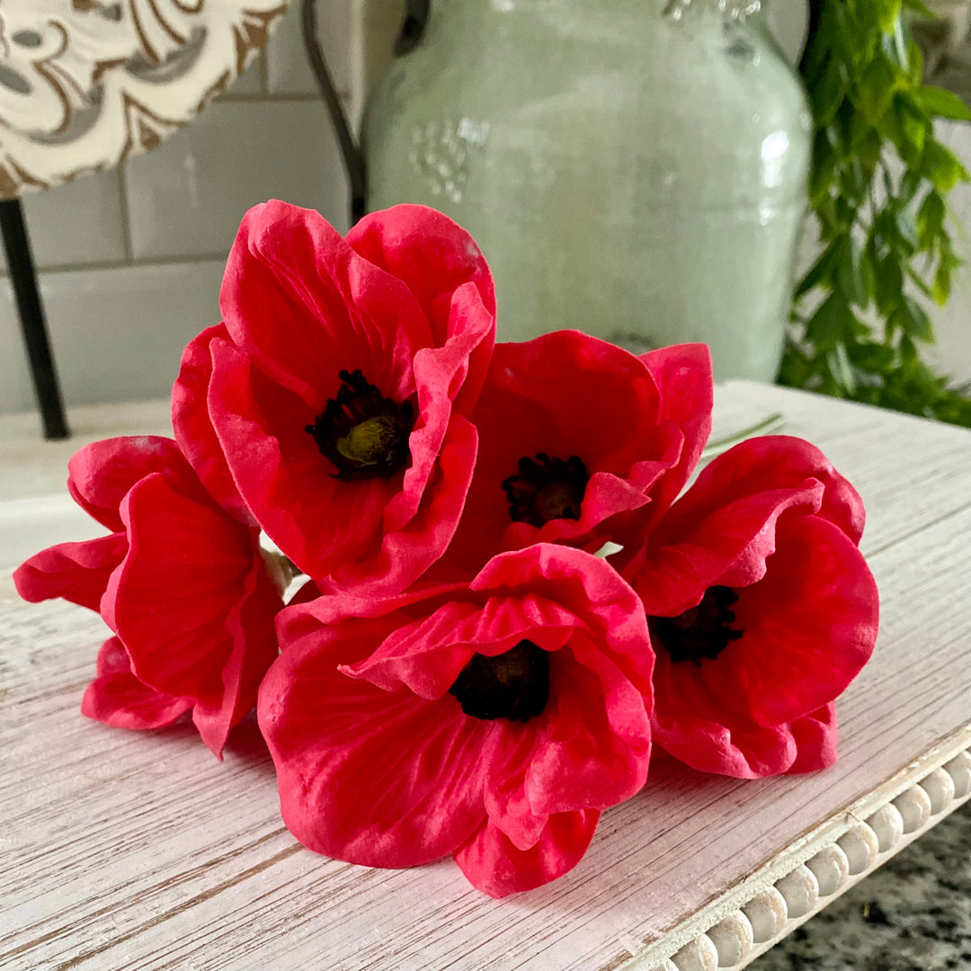 A bundle of artificial red poppy flowers tied with raffia, displayed on a wooden surface.