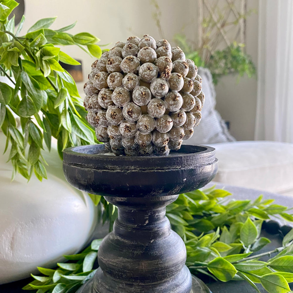A handcrafted decorative weathered berry orb with an olive-green hue, intended to be used as a bowl filler.