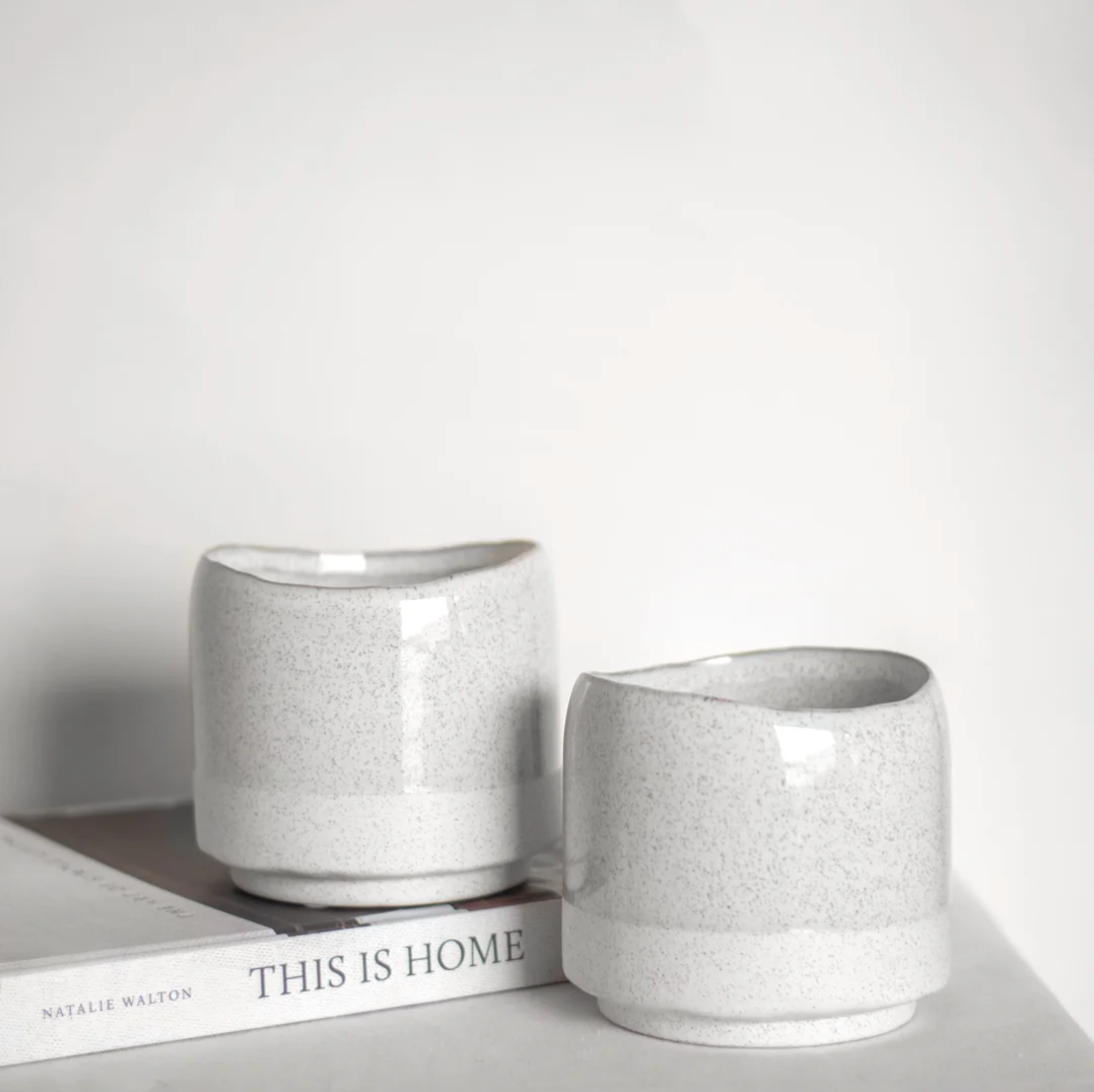 Ceramic soy wax candles with a vanilla and white tea scents, in cream and gray color block speckled finish, displayed on a book.