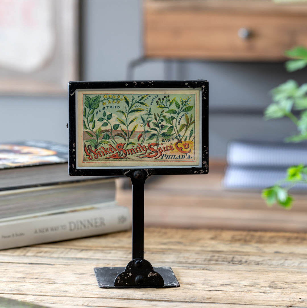 A vintage-style metal bin photo frame with a distressed black paint finish holding a photo, placed on a wooden surface.