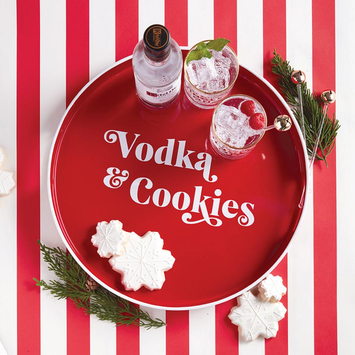 A red round serving tray with 'Vodka & Cookies' text, accompanied by a glass of vodka with ice and a cherry, and two cookies shaped like snowflakes.