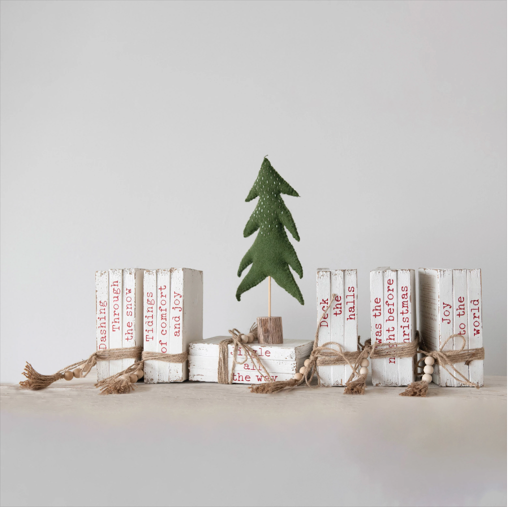 A decorative wooden book block with a Christmas tree on top, tied with jute to a distressed white finish.