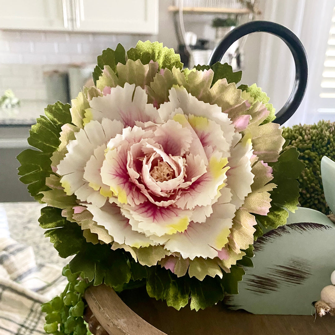 A artificial pink potted cabbage plant with green and white leaves, placed in a brown pot with a pink ombre finish.